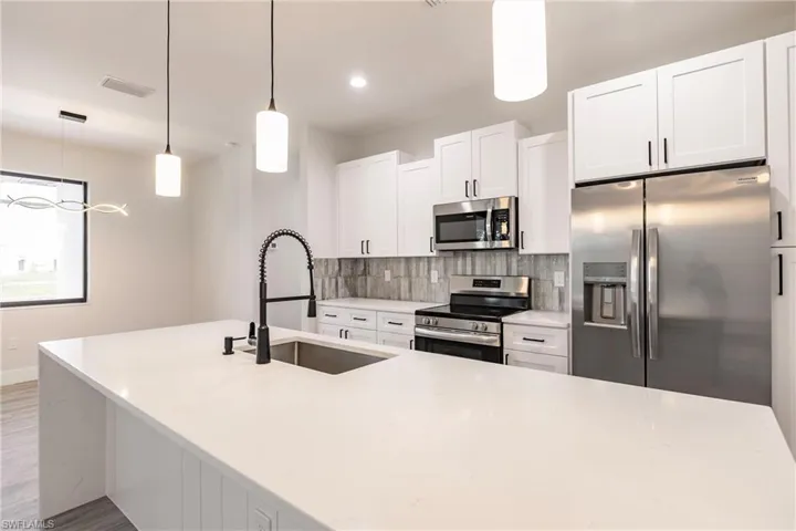 Kitchen featuring hanging light fixtures, sink, tasteful backsplash, appliances with stainless steel finishes, and light hardwood / wood-style floors