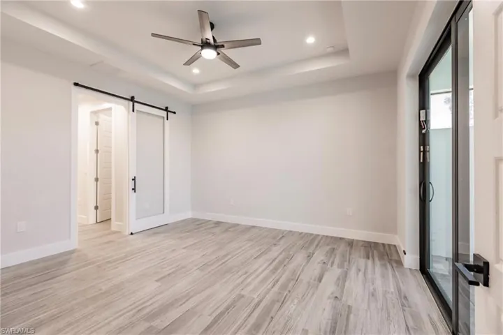 Empty room featuring ceiling fan, a tray ceiling, a barn door, and light hardwood / wood-style flooring