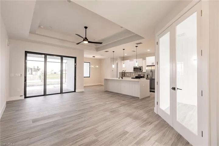Unfurnished living room featuring a raised ceiling, sink, light wood-type flooring, and ceiling fan