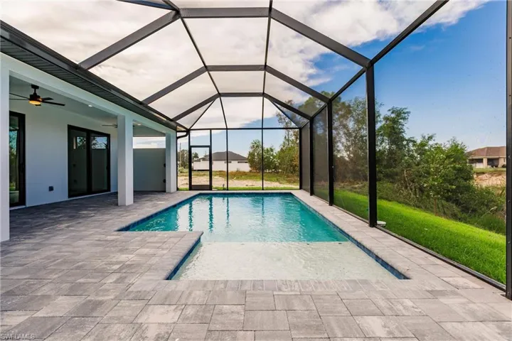 View of pool with glass enclosure, a patio area, and ceiling fan