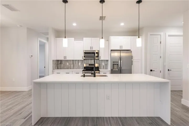 Kitchen with white cabinets, a center island with sink, appliances with stainless steel finishes, and sink