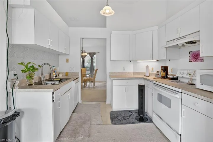 Kitchen featuring white appliances, light countertops, under cabinet range hood, white cabinetry, and decorative light fixtures