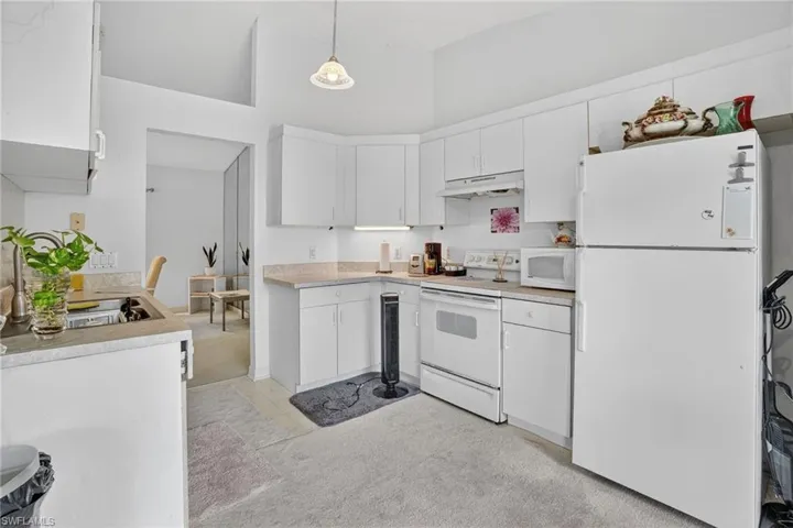 Kitchen featuring white appliances, light countertops, high vaulted ceiling, hanging light fixtures, and white cabinets