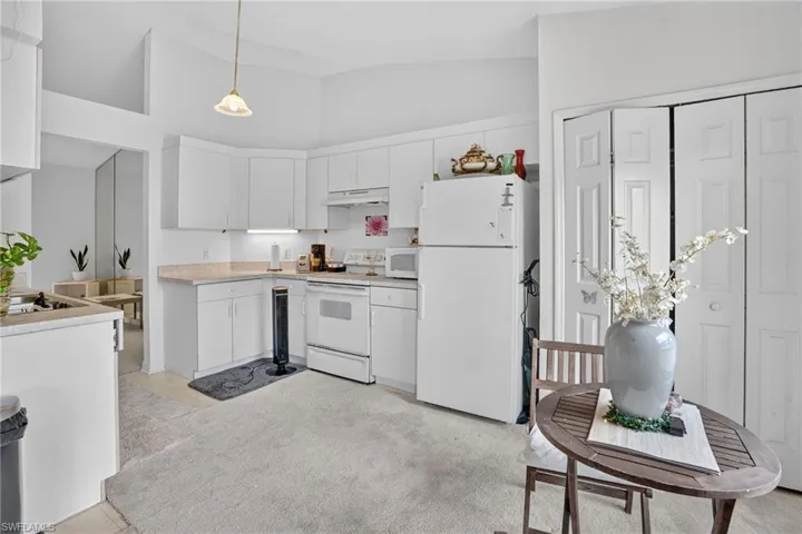 Kitchen featuring light countertops, white appliances, high vaulted ceiling, hanging light fixtures, and white cabinets