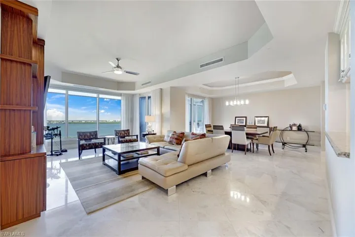 Expansive open-concept living area featuring polished stone flooring, floor-to-ceiling windows with panoramic vistas, coffered ceiling with recessed lighting, and a ceiling fan