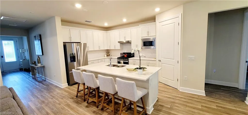 Kitchen featuring appliances with stainless steel finishes, light wood-type flooring, white cabinetry, and a kitchen island with sink