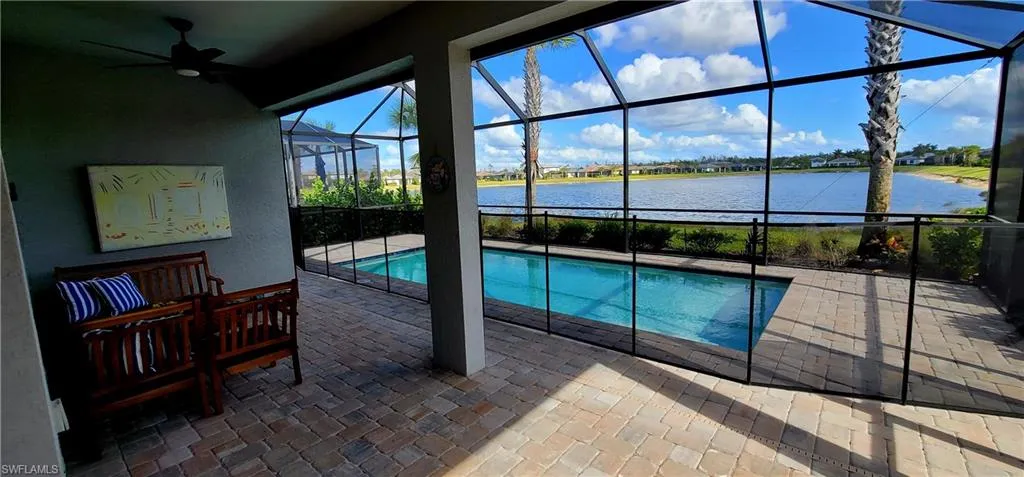 View of pool with glass enclosure, ceiling fan, a water view, and a patio