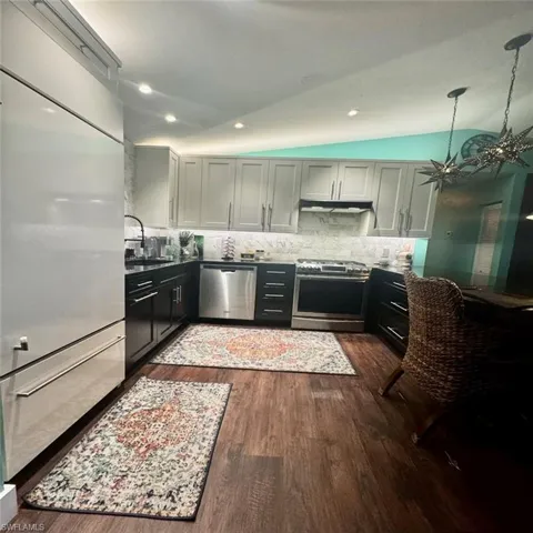 Kitchen with vaulted ceiling, a notable chandelier, sink, dark hardwood / wood-style floors, and appliances with stainless steel finishes