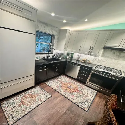 Kitchen featuring vaulted ceiling, dark hardwood / wood-style floors, sink, and appliances with stainless steel finishes