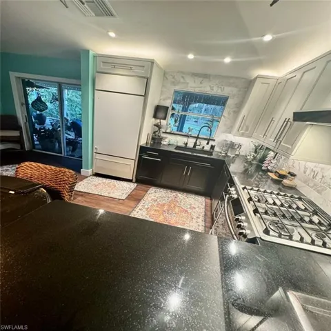 Kitchen with hardwood / wood-style floors, stainless steel gas cooktop, white cabinetry, and sink