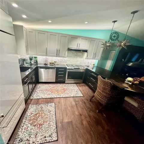 Kitchen with stainless steel appliances, dark hardwood / wood-style flooring, pendant lighting, decorative backsplash, and vaulted ceiling