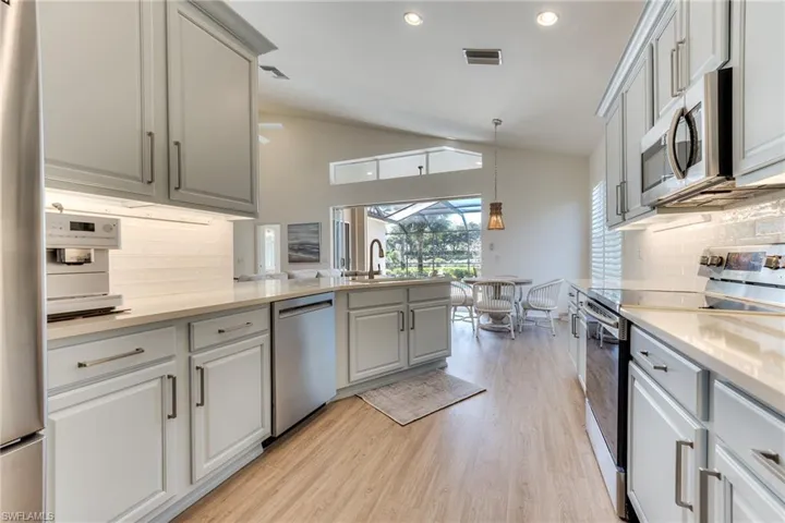 Kitchen with light wood finished floors, lofted ceiling, visible vents, appliances with stainless steel finishes, and a sink