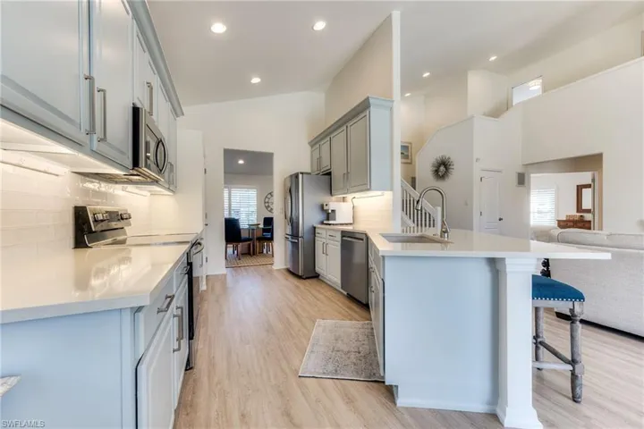 Kitchen featuring a kitchen breakfast bar, a peninsula, stainless steel appliances, gray cabinetry, and a sink