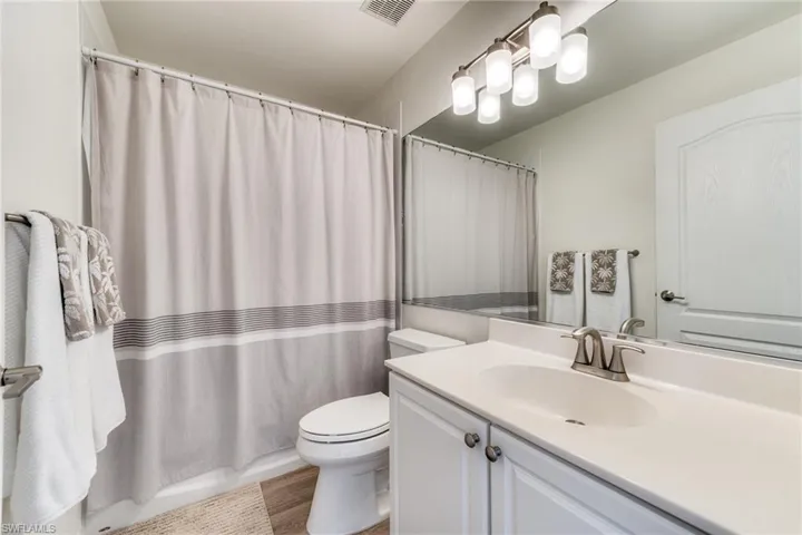 Full bathroom with toilet, visible vents, a shower with shower curtain, and vanity