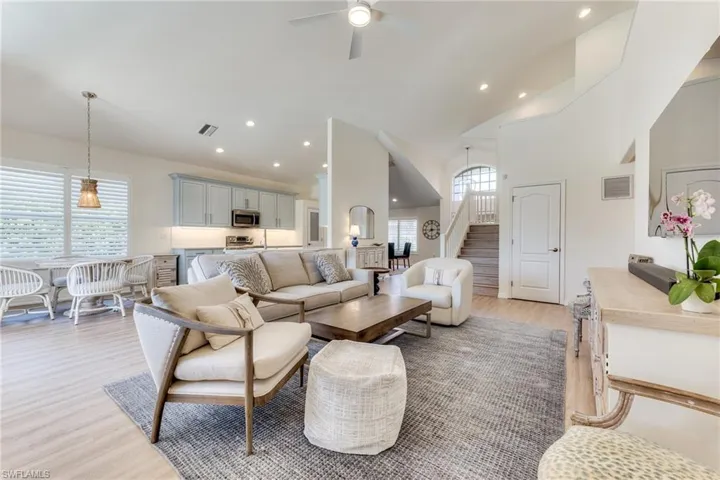 Living area featuring visible vents, a ceiling fan, stairs, light wood-style floors, and high vaulted ceiling