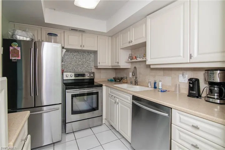Kitchen with stainless steel appliances, a sink, light tile patterned flooring, a tray ceiling, and light countertops