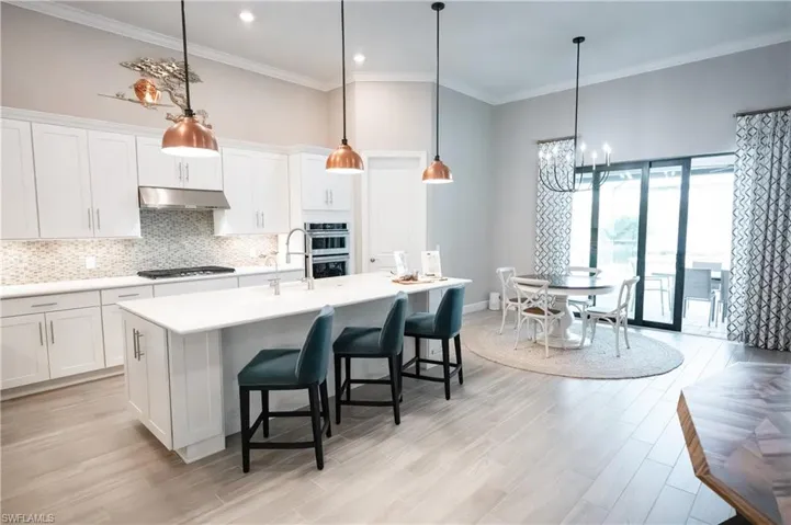 Kitchen with white cabinets, stainless steel appliances, an island with sink, a kitchen breakfast bar, and hanging light fixtures