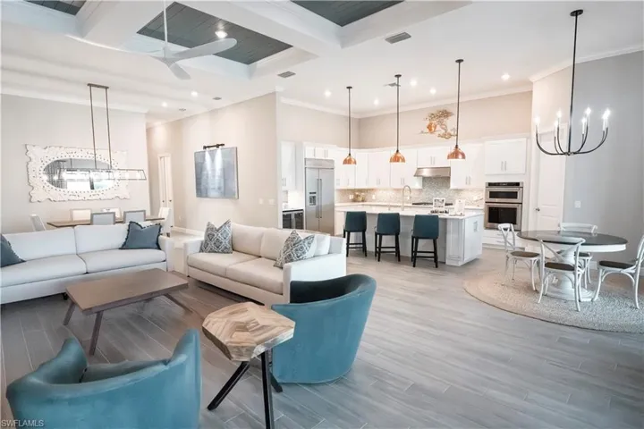 Living room featuring ceiling fan with notable chandelier, beamed ceiling, ornamental molding, light wood-type flooring, and coffered ceiling