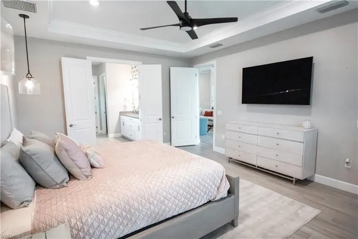 Bedroom featuring ensuite bath, light hardwood / wood-style floors, ornamental molding, a raised ceiling, and ceiling fan