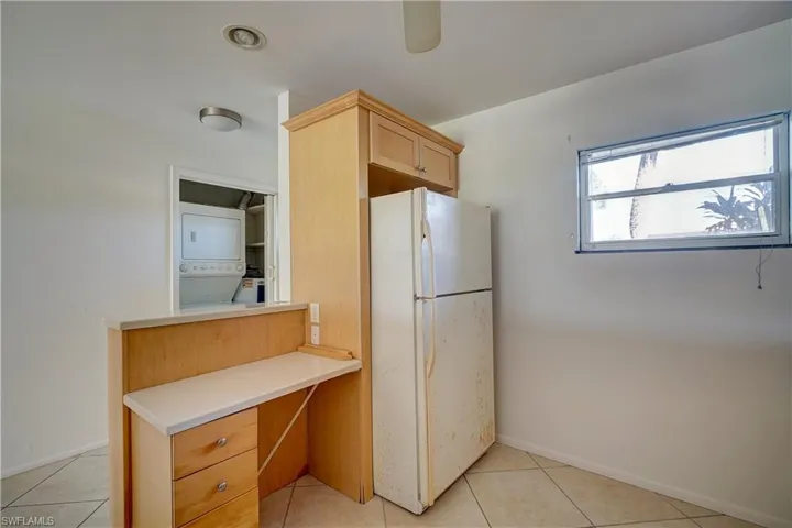 Kitchen with stacked washing maching and dryer, light tile patterned flooring, and white refrigerator