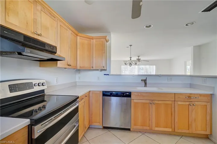 Kitchen with exhaust hood, sink, light tile patterned flooring, decorative light fixtures, and appliances with stainless steel finishes