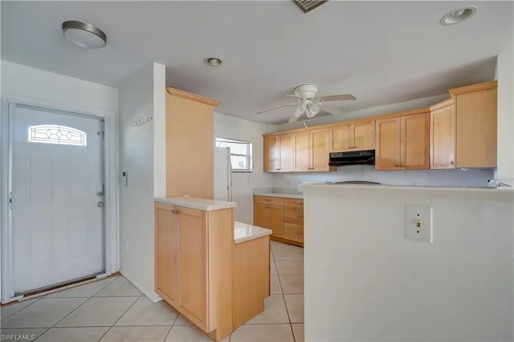 Kitchen with light brown cabinets, light tile patterned flooring, kitchen peninsula, and ceiling fan
