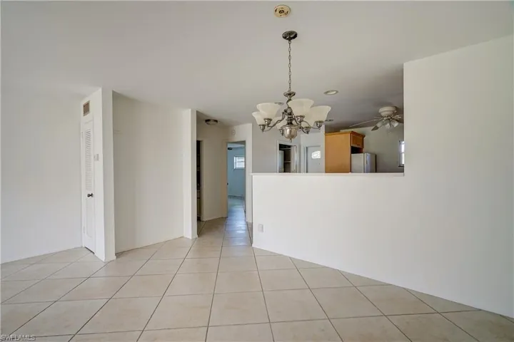 Tiled spare room featuring ceiling fan with notable chandelier