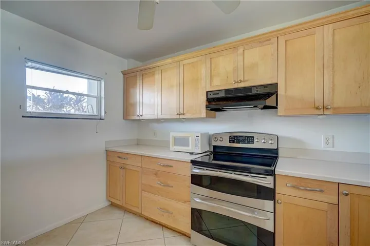 Kitchen featuring ceiling fan, light brown cabinetry, light tile patterned floors, and stainless steel electric range oven