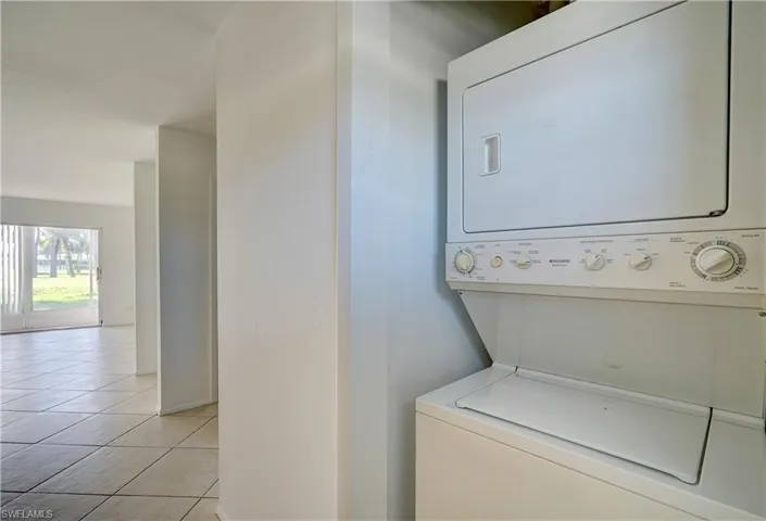 Washroom with stacked washer and clothes dryer and light tile patterned floors