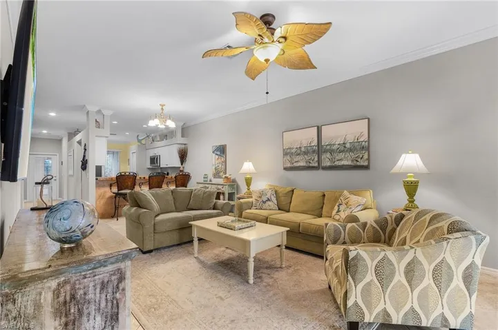 Living room with crown molding and ceiling fan with notable chandelier