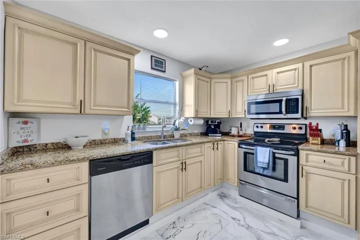 Kitchen featuring cream cabinets, stainless steel appliances, light stone countertops, and light marble finish flooring