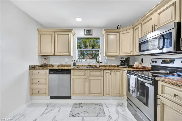Kitchen featuring stainless steel appliances, cream cabinetry, dark stone countertops, and light marble finish floors