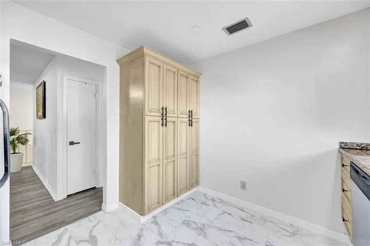 Kitchen featuring light marble finish floors, stainless steel dishwasher, light wood finish cabinetry, and light stone countertops