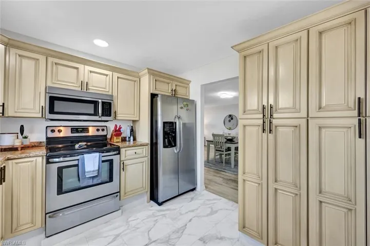 Kitchen featuring cream cabinets, stainless steel appliances, light marble finish flooring, light stone counters, and recessed lighting
