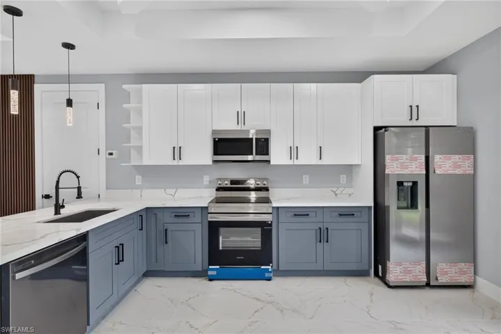 Modern kitchen featuring white and blue-grey cabinetry, stainless steel appliances, and white marble-look countertops