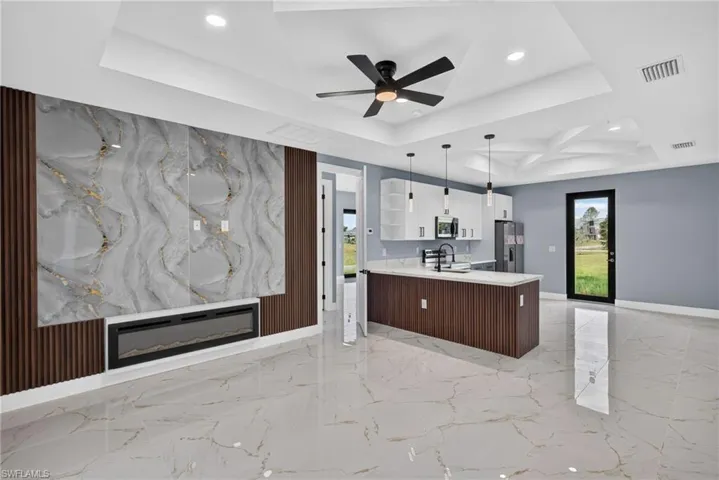 Open-concept living space featuring large-format tile flooring, a decorative wall panel with an integrated linear electric fireplace, and a tray ceiling with recessed lighting