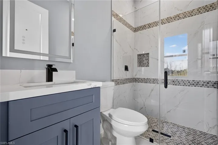 Contemporary bathroom featuring a floating vanity with a white countertop and integrated sink, a sleek black faucet, and an illuminated mirror