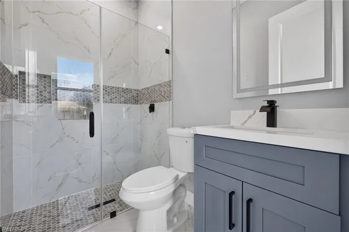 Walk-in shower with clear glass enclosure, white marble-look tile, and a mosaic accent band