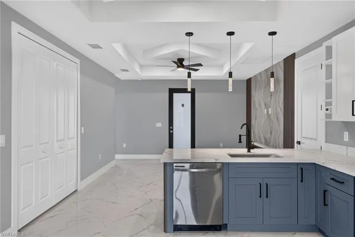 Modern kitchen featuring blue shaker-style base cabinetry with black hardware, white upper cabinets, and a stainless steel dishwasher