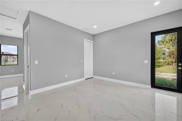 Spacious room featuring large format tile flooring, a black-framed glass-paneled exterior door, a white interior door, and recessed lighting