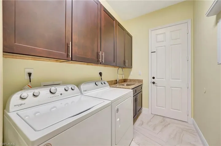 Clothes washing area featuring washer and clothes dryer, cabinets, and sink