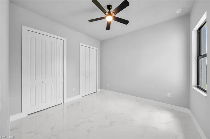 Unfurnished bedroom with multiple closets, light marble finish floors, and ceiling fan