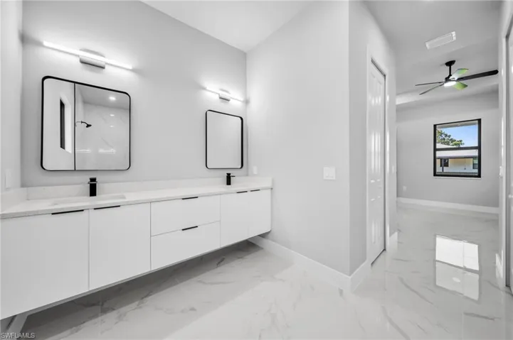 Bathroom featuring double vanity, a marble finish shower, light marble finish floors, and a ceiling fan