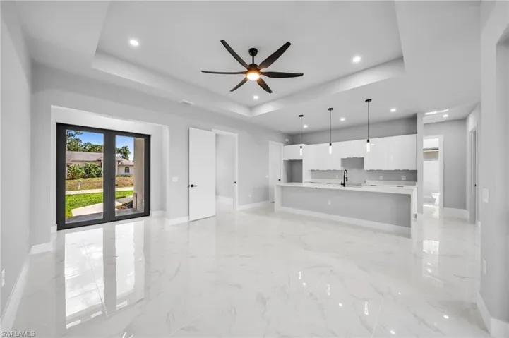 Unfurnished living room with light marble finish floors, a raised ceiling, a ceiling fan, and recessed lighting