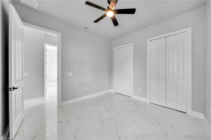 Unfurnished bedroom with two closets, light marble finish floors, and ceiling fan