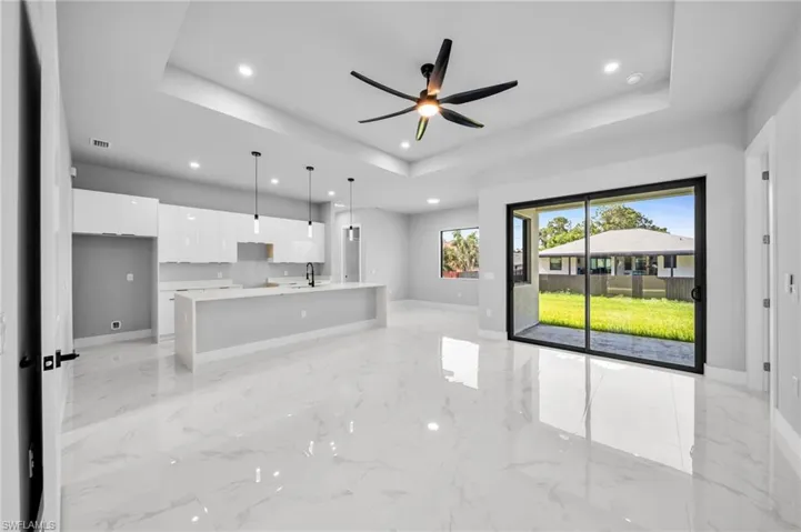 Unfurnished living room featuring a ceiling fan, recessed lighting, a tray ceiling, and light marble finish flooring