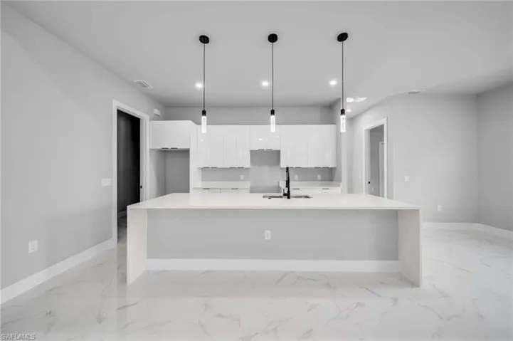 Kitchen with modern cabinets, white cabinetry, light stone counters, recessed lighting, and a large island with sink