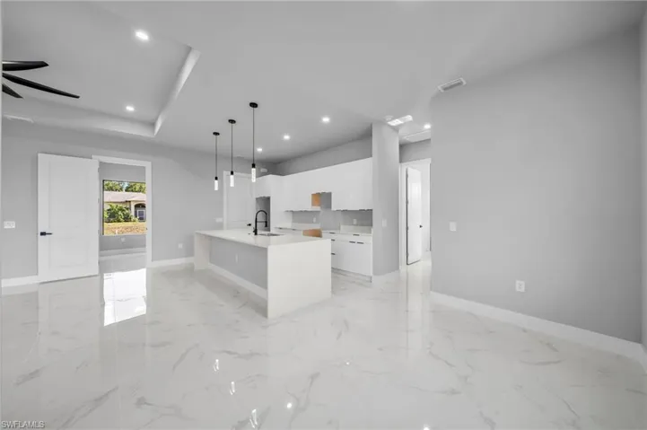 Kitchen featuring white cabinets, pendant lighting, recessed lighting, light stone counters, and an island with sink
