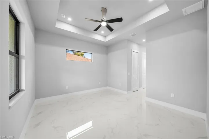 Spare room with a raised ceiling, light marble finish floors, recessed lighting, and ceiling fan