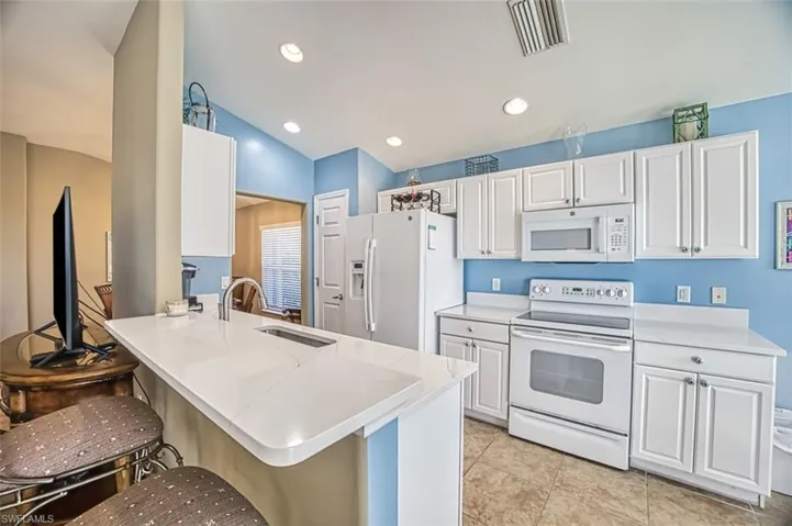 Kitchen featuring white appliances, white cabinets, a kitchen breakfast bar, lofted ceiling, and a peninsula